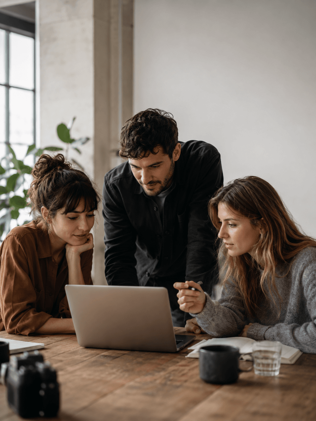 A small team gathered around a laptop, reviewing work together in a studio setting.